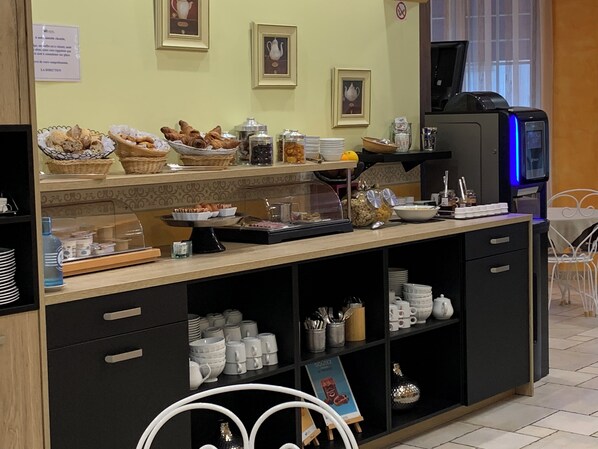 Zona de buffet con diferentes opciones de comida, una máquina de café y una exhibición de tazas y vasos.