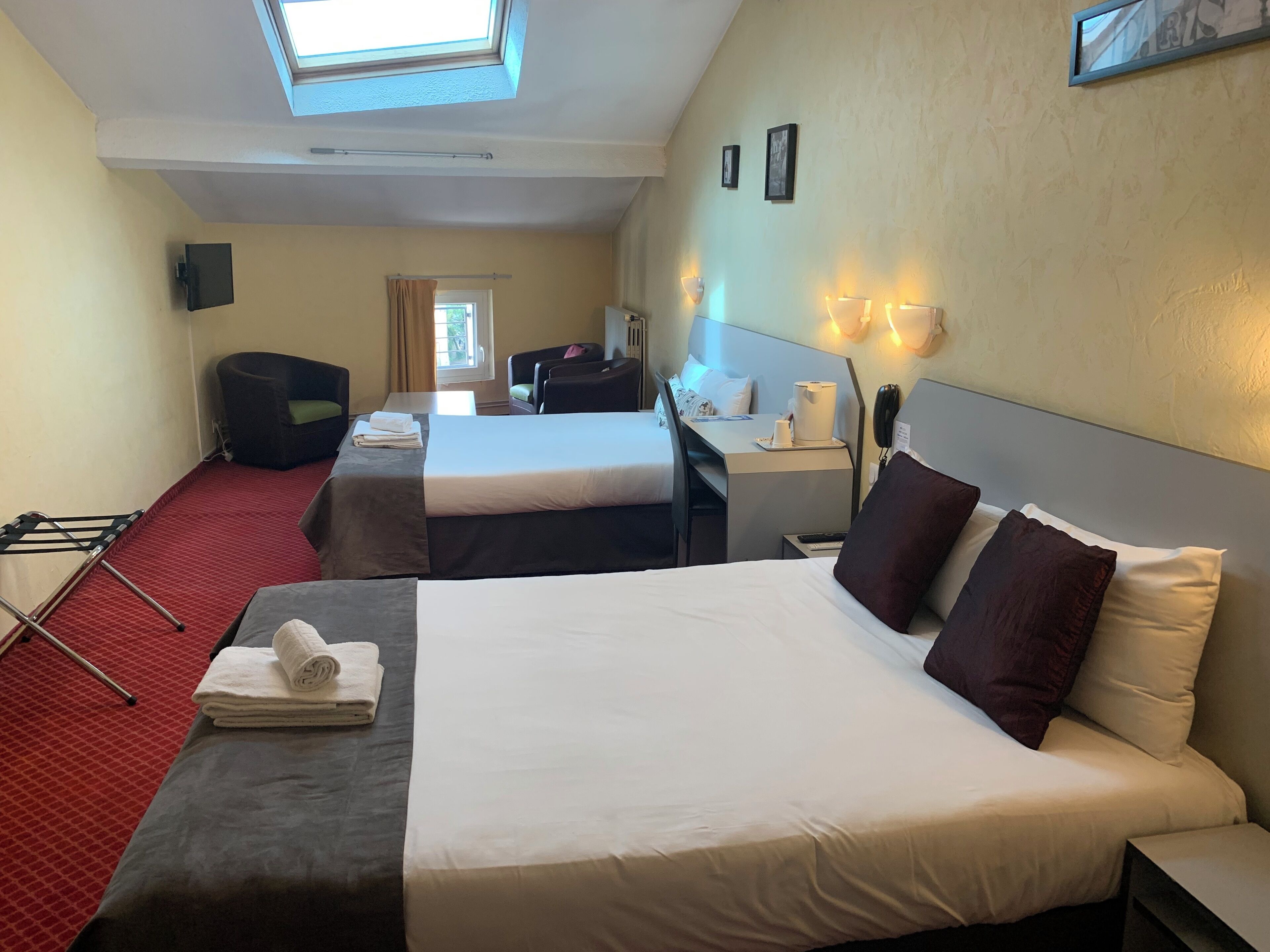 A hotel room with two beds, a desk, a chair, a TV, and a skylight.