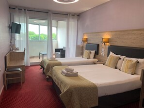 A hotel room with two beds, a desk, a chair, a TV, and a view of greenery outside. - Brit Hotel Bleu Nuit (Saintes)