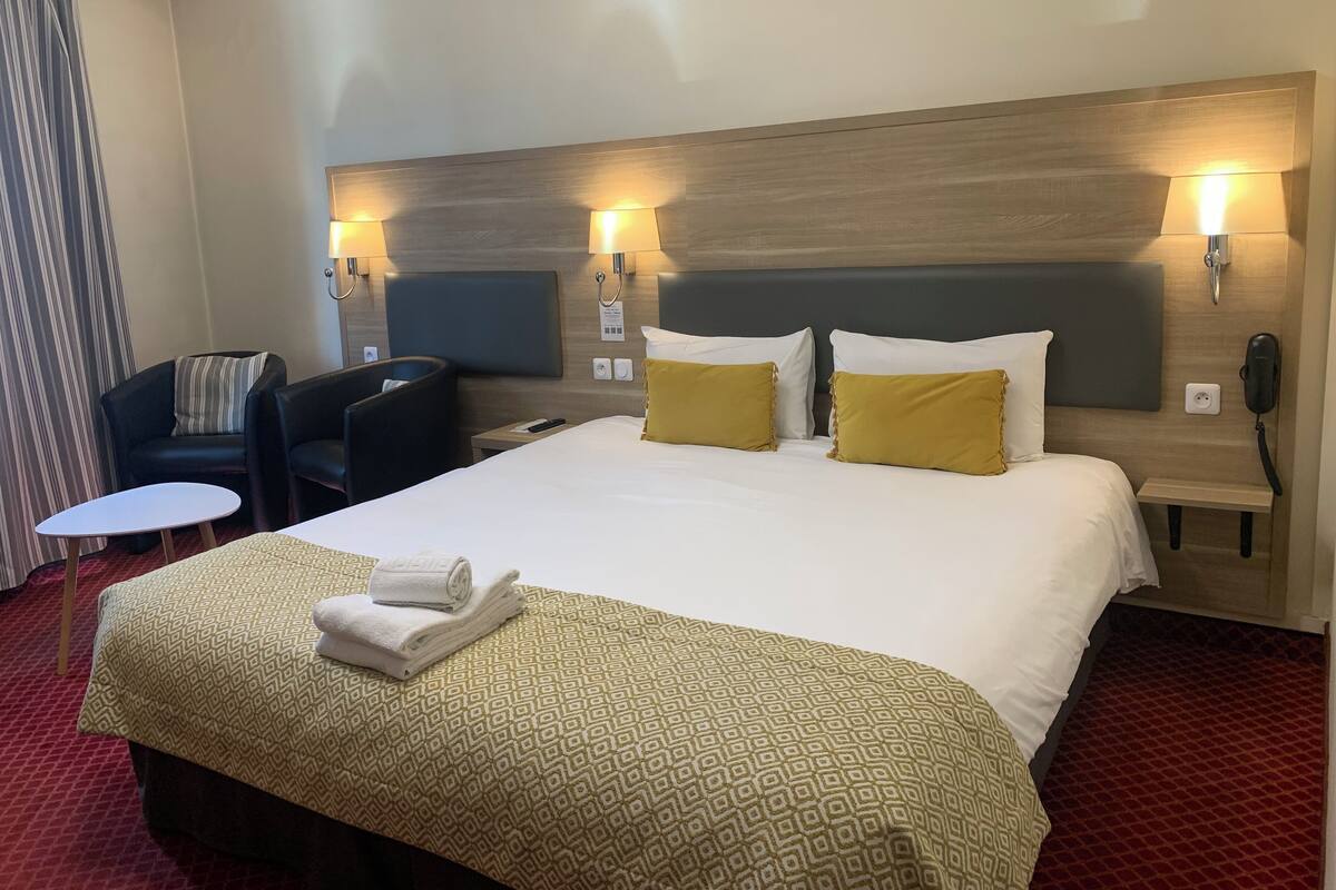 A hotel room with a large bed, two bedside lamps, a desk, a chair, and a small table.