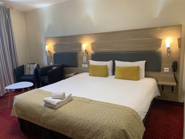 Una habitación de hotel con una cama grande, dos lámparas de noche, un escritorio, una silla y una mesita.