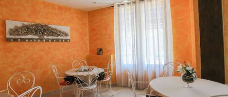 A dining area with a table and chairs, a painting on the wall, and a window with curtains.