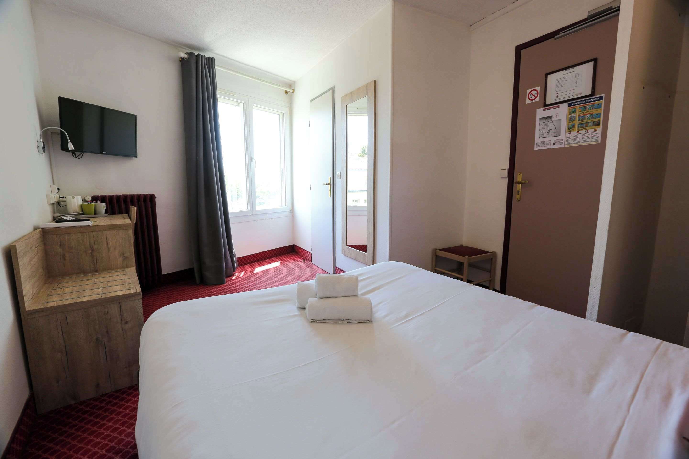 Ett hotellrum med en stor säng, en träbänk, en tv som är monterad på väggen och en dörr där olika anslag är upphängda.