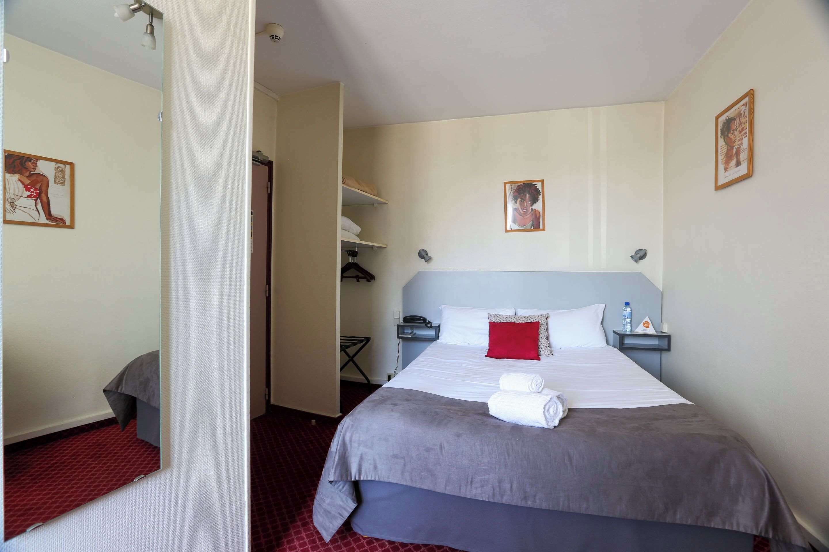 Habitación de hotel con cama, mesita de noche, espejo y puerta que da a un pasillo.
