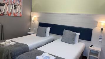 Une chambre d’hôtel avec deux lits, chacun muni d’un oreiller et d’une serviette roulée. On y trouve une petite table de chevet avec une lampe et une télécommande.