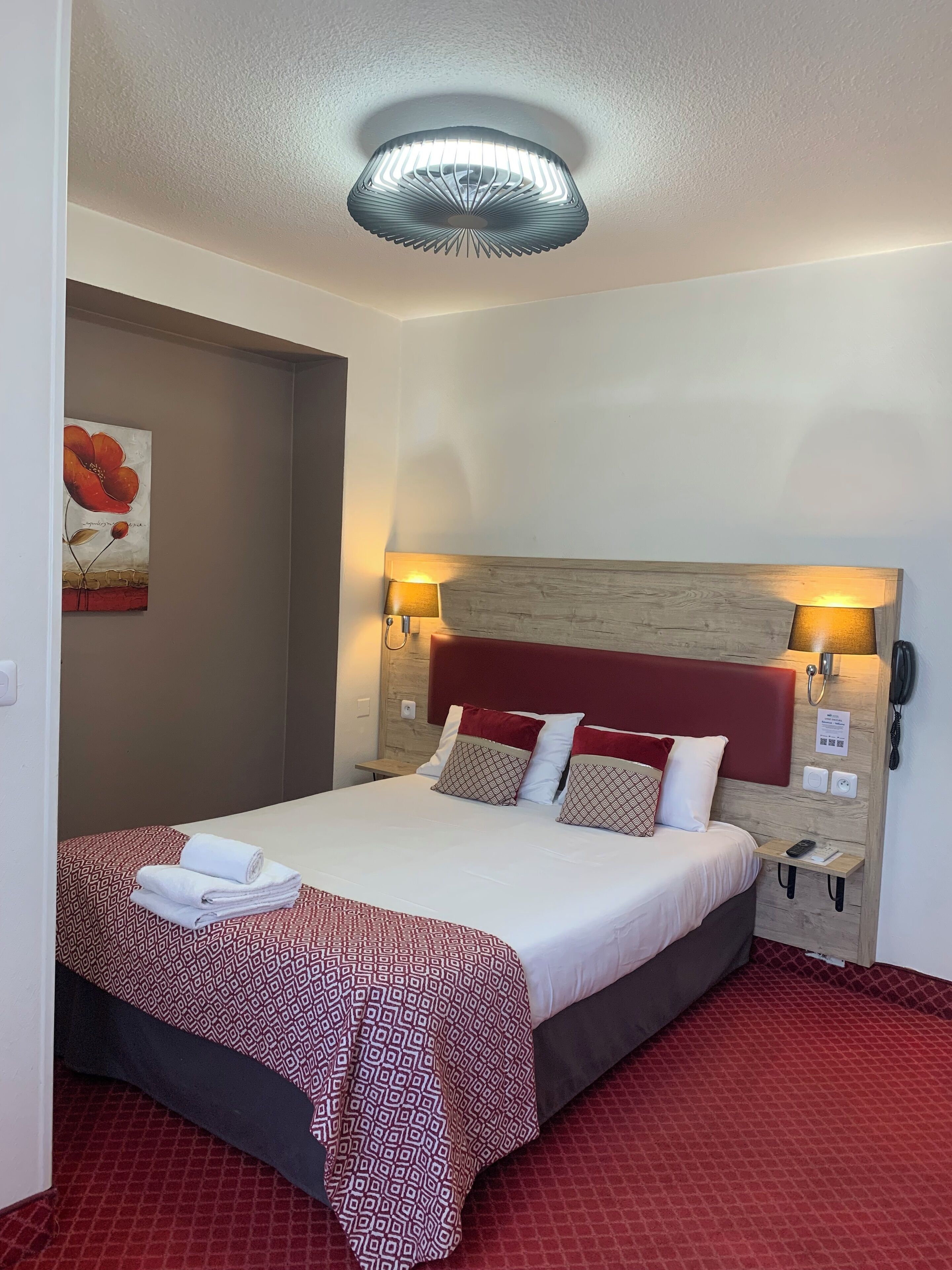 Habitación de hotel con cama, cabecera, dos lámparas de noche, mesita de noche y teléfono fijo en la pared.