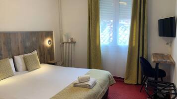 A hotel room with a bed, a desk, a chair, a TV, and a window with curtains.