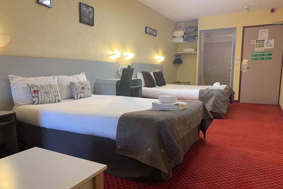 A hotel room with two beds, a desk, a chair, a red carpet, and a door with a sign.
