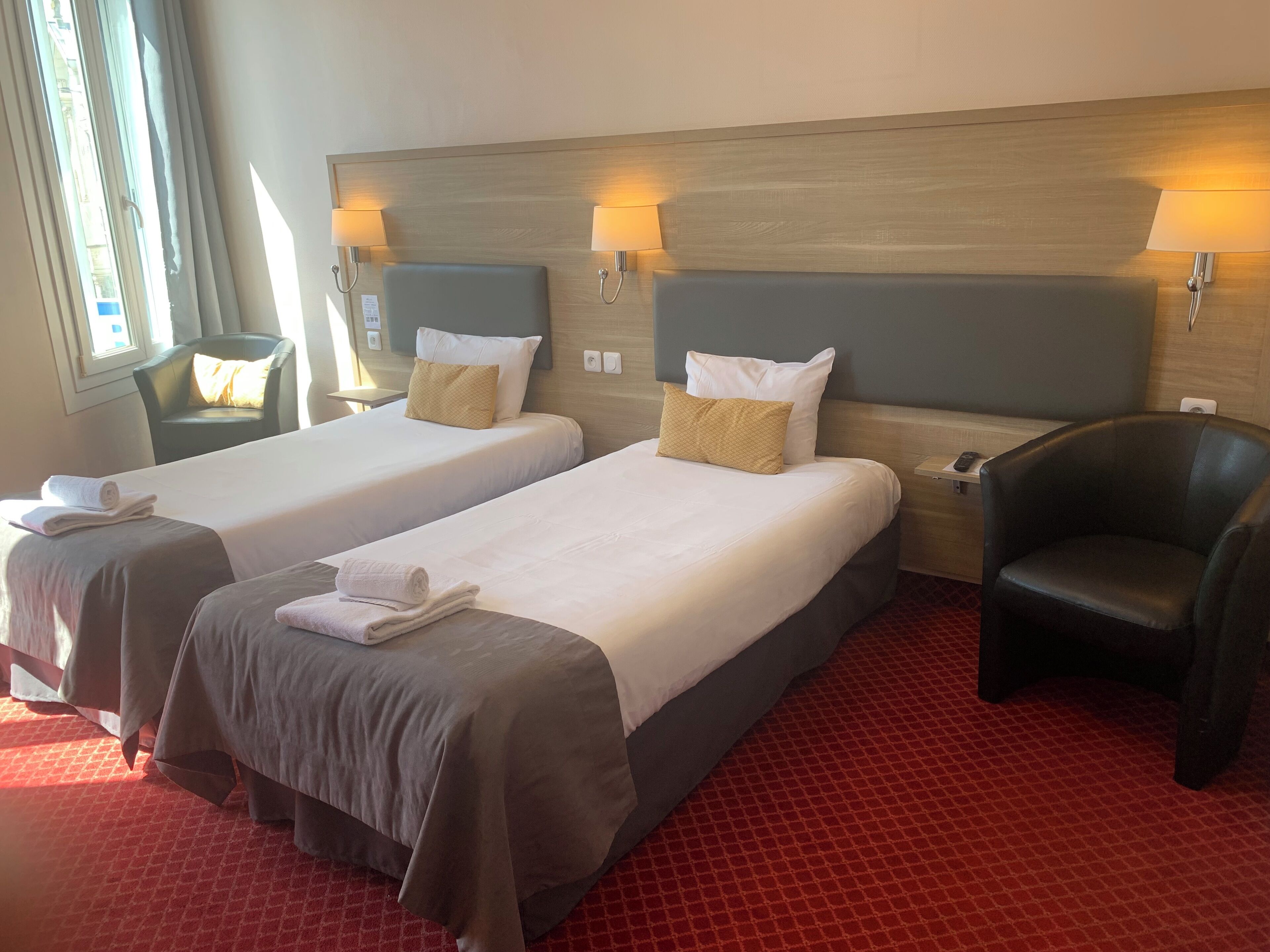 A hotel room with two beds, each with a headboard, bedside lamps, and towels.