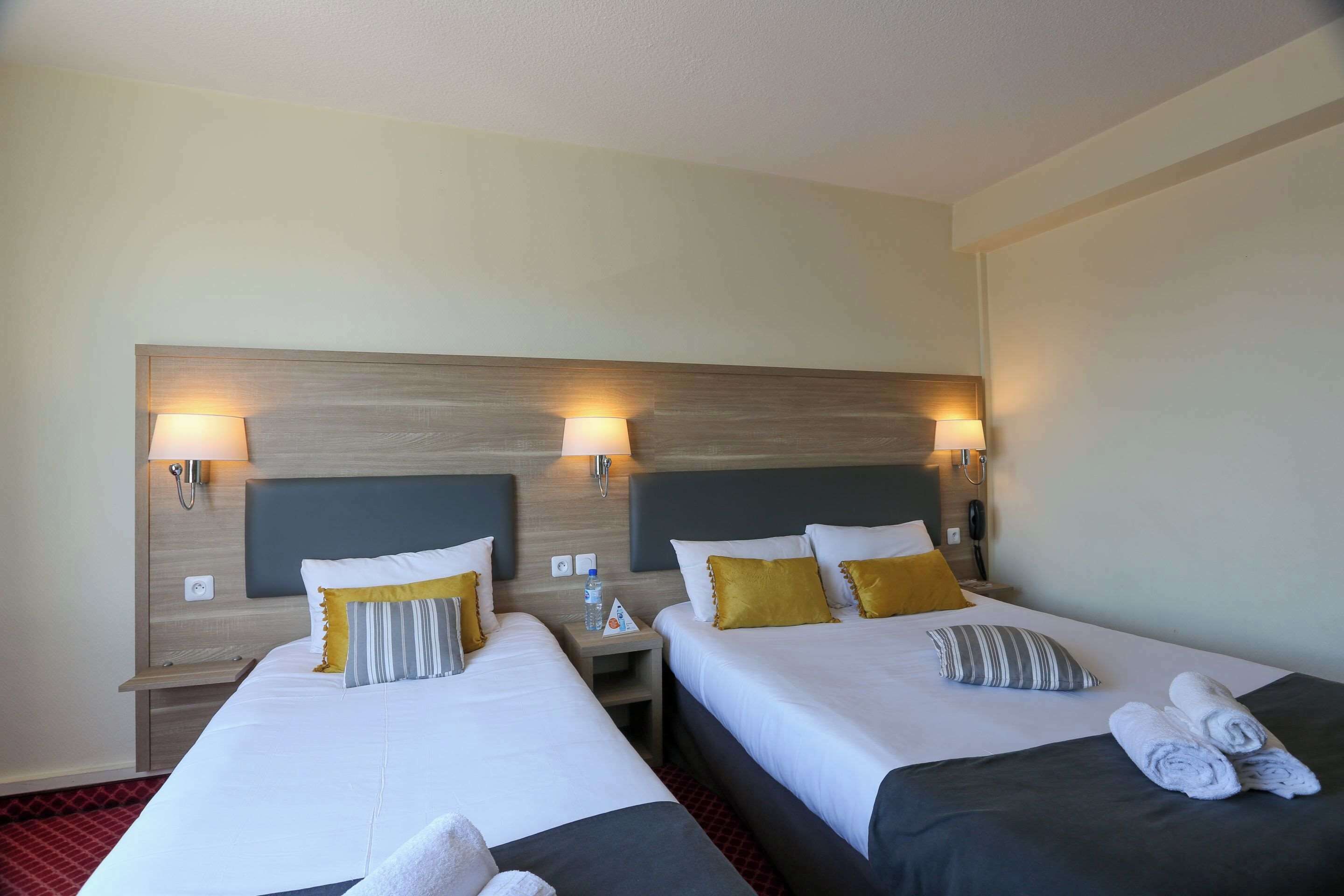 Ett hotellrum med två sängar, var och en med en sänggavel, sängbord, lampor och handdukar.