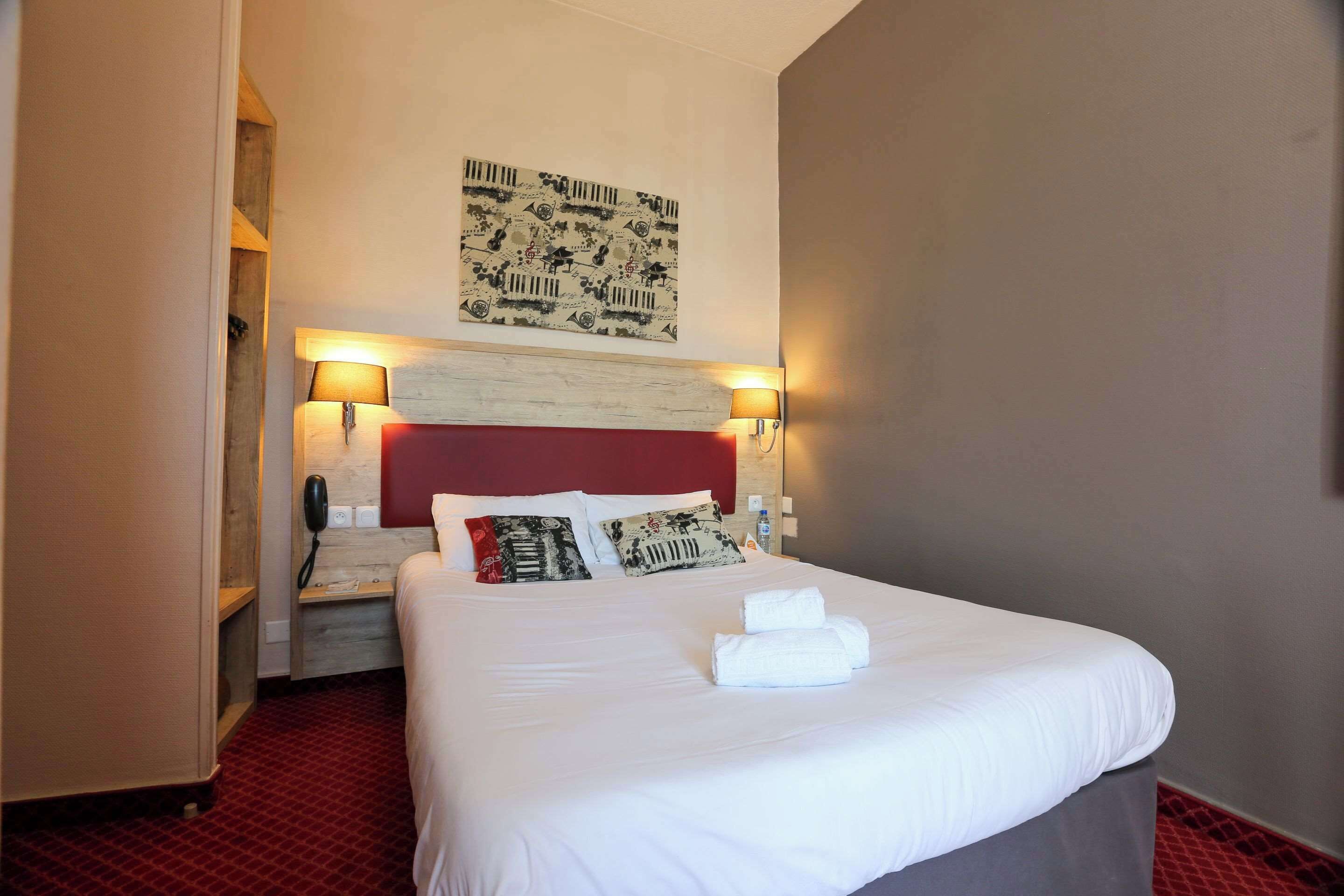 Une chambre d’hôtel avec un lit bien fait, un téléphone, une lampe fixée au mur et une œuvre d’art décorative au-dessus du lit.