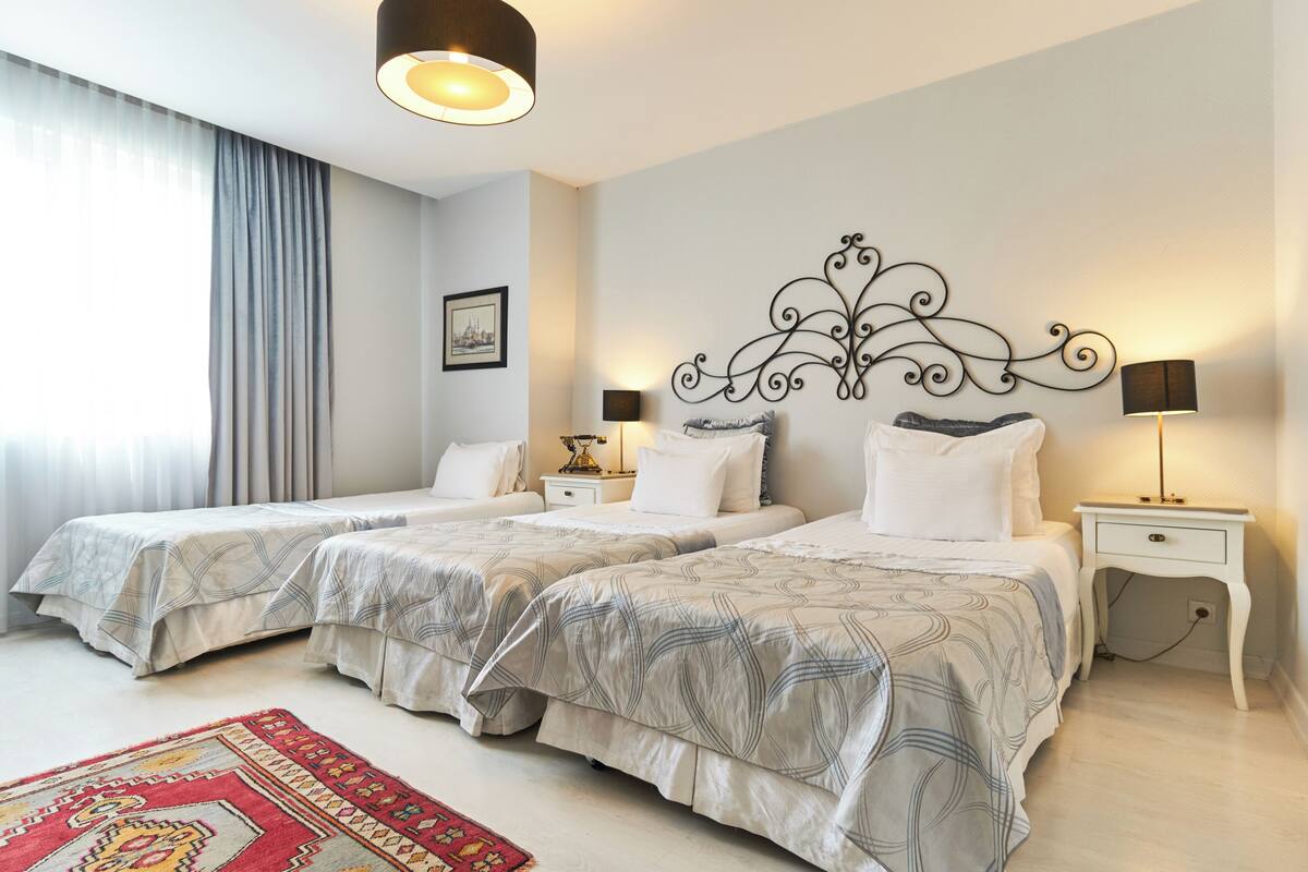 A hotel room with two beds, a red patterned rug, and a decorative wall piece.