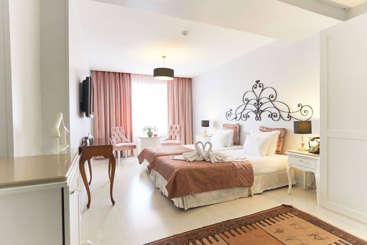 A hotel room with two beds, a desk, a chair, a TV, and a decorative wall piece.