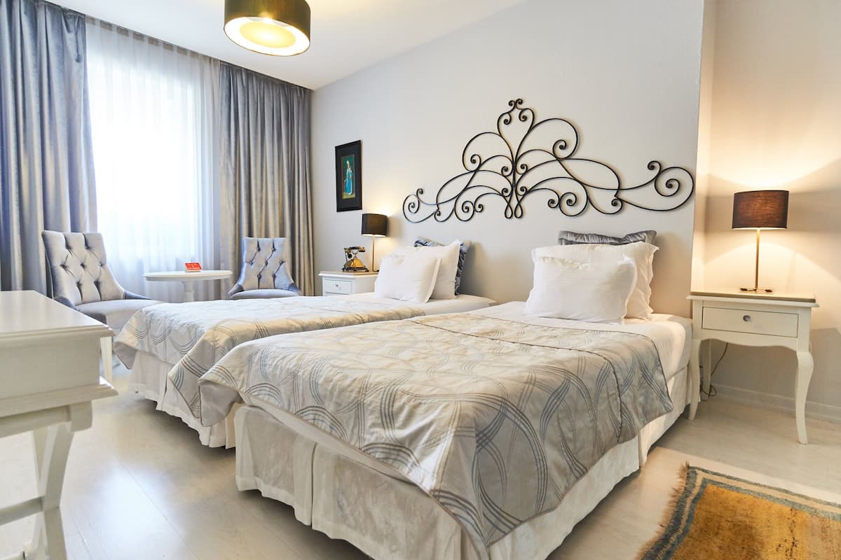 A hotel room with two beds, a desk, a chair, a lamp, and a decorative wall piece.