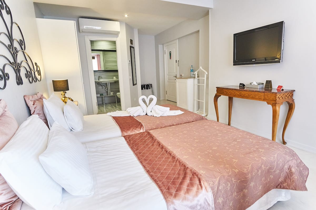 A hotel room with a bed, a TV, a desk, and a bathroom visible through an open door.