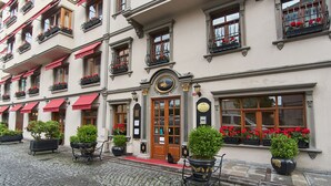 A historic building with a central entrance, multiple windows with flower boxes, and potted plants on the ground.