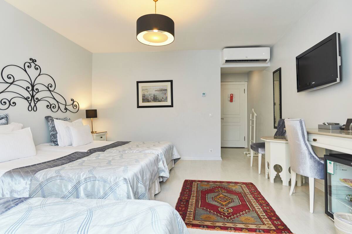 A hotel room with two beds, a desk, a chair, an air conditioner, a television, and a framed picture on the wall.