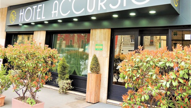 Un hotel llamado "HOTEL ACCURSIO" con una fachada moderna, ventanas amplias y plantas en macetas al frente.