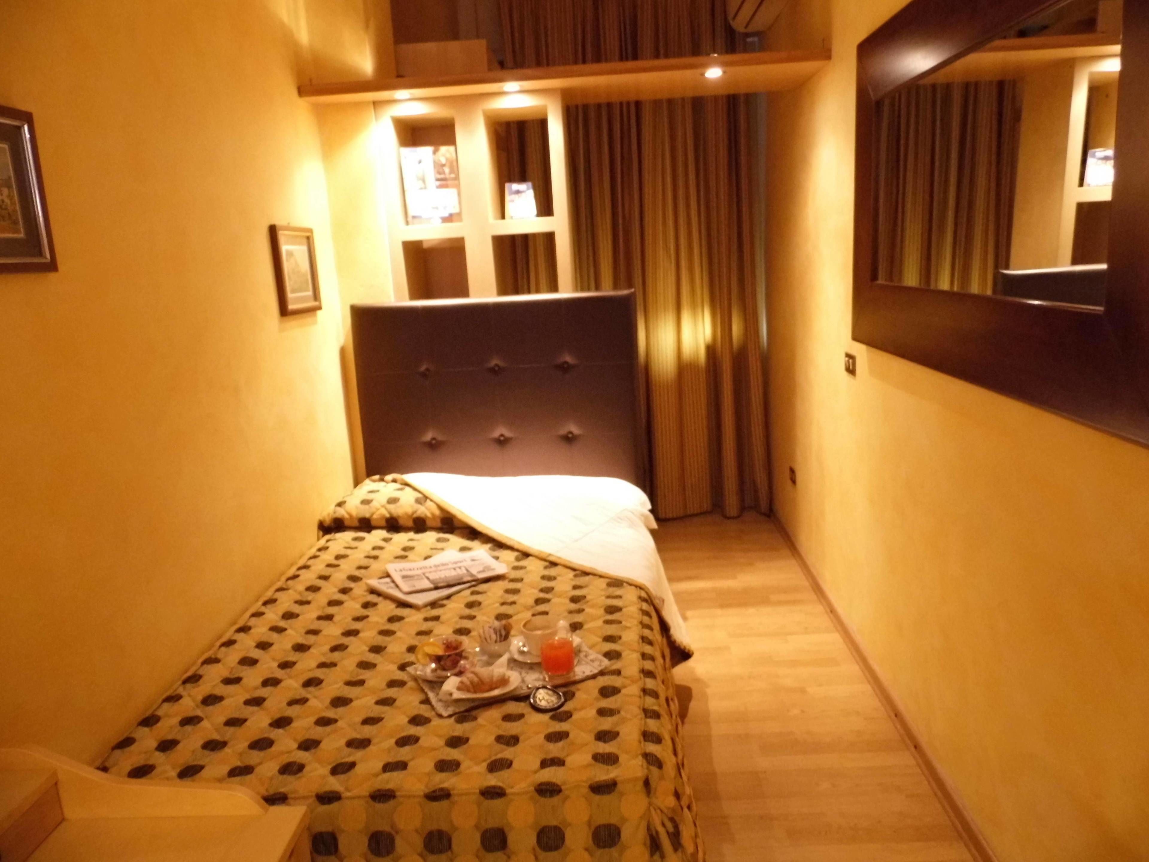 Una habitación de hotel con cama, mesita de noche con una bandeja de desayuno, espejo y cortina.