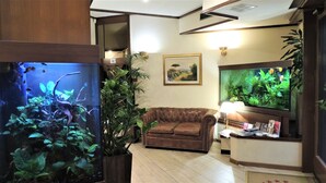 Una habitación con un acuario grande, un sofá de cuero marrón, un escritorio con una lámpara y un cuadro en la pared.