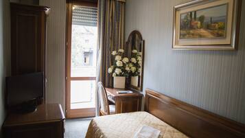 A hotel room with a bed, a television, a desk with a mirror, and a painting on the wall.