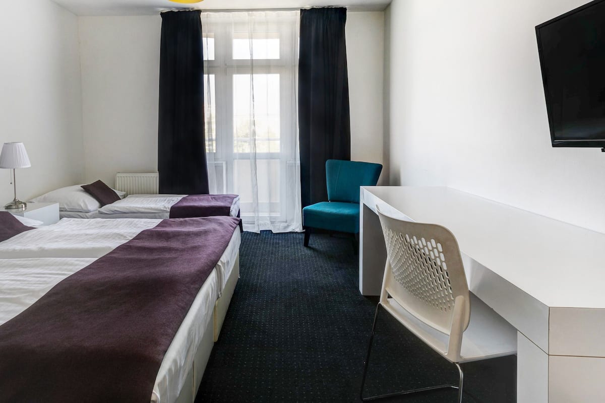 A hotel room with two beds, a desk, a chair, a TV, and a window with curtains.