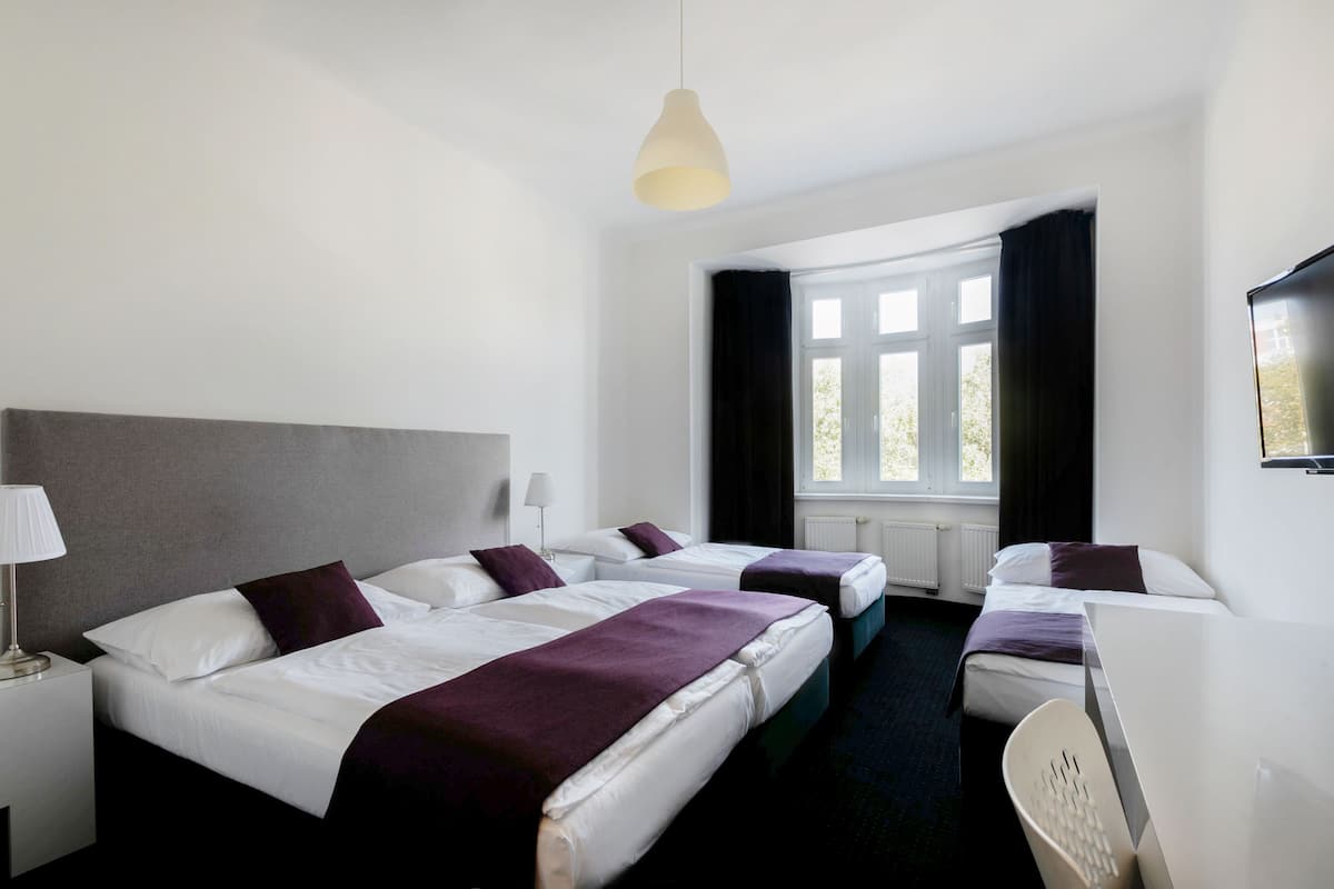 A hotel room with two beds, a desk, a chair, a lamp, and a TV.