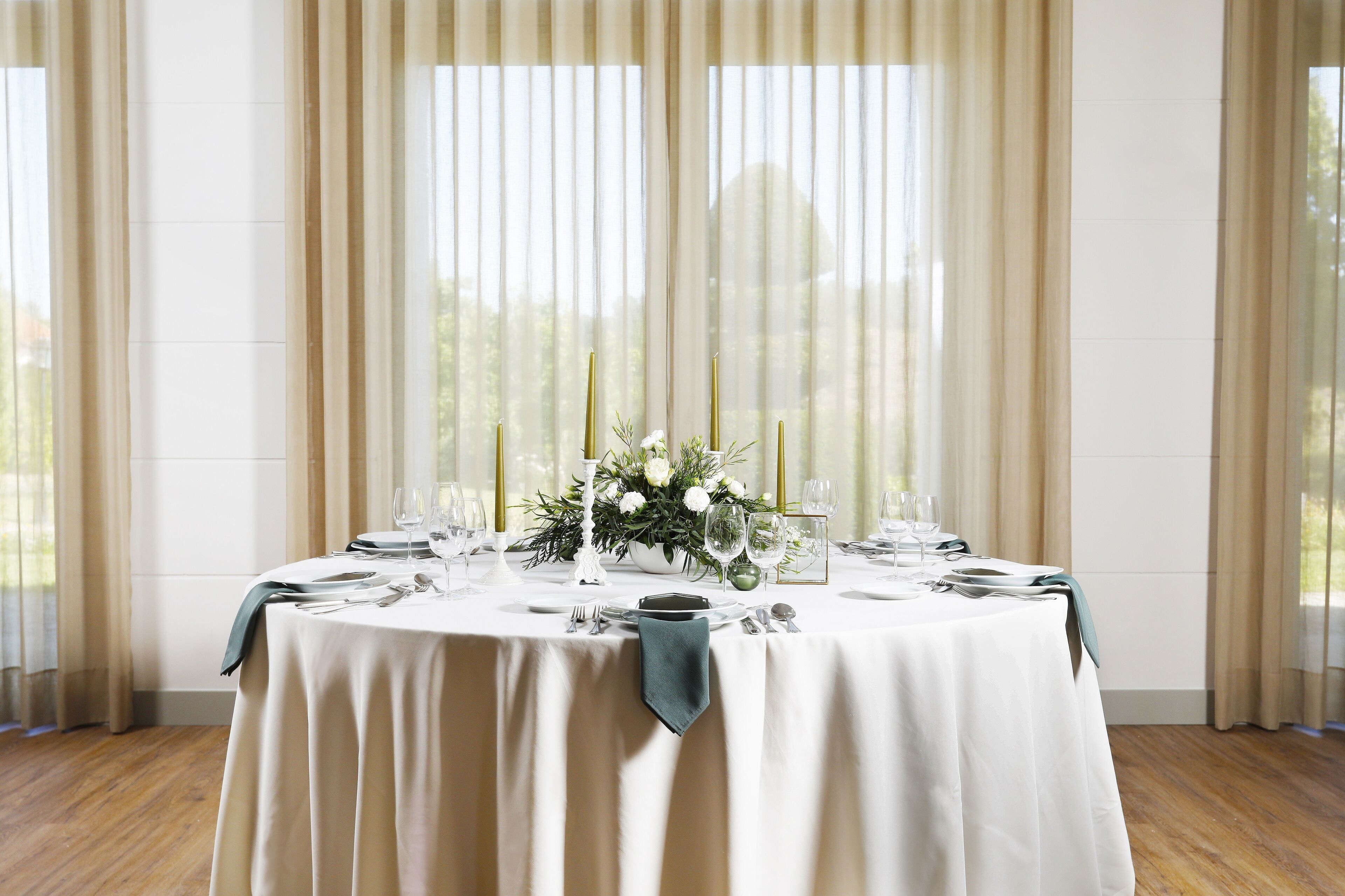 A round table set for a meal with a white tablecloth, candles, and a floral centerpiece.
