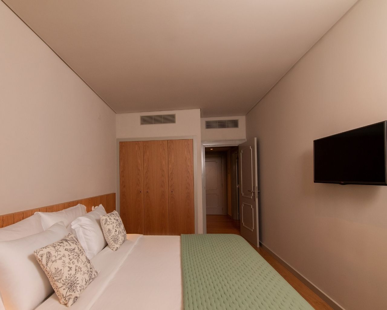A hotel room with a bed, a television, a wardrobe, and a door leading to another room.