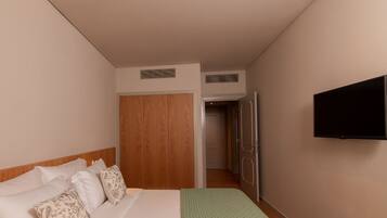 A hotel room with a bed, a television, a wardrobe, and a door leading to another room.