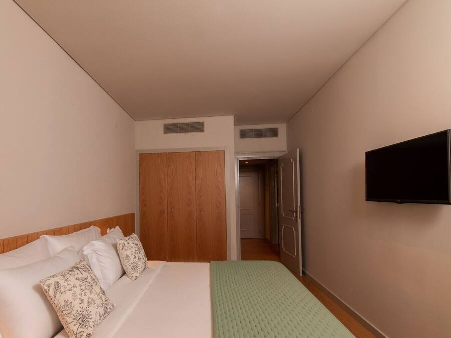 A hotel room with a bed, a television, a wardrobe, and a door leading to another room.