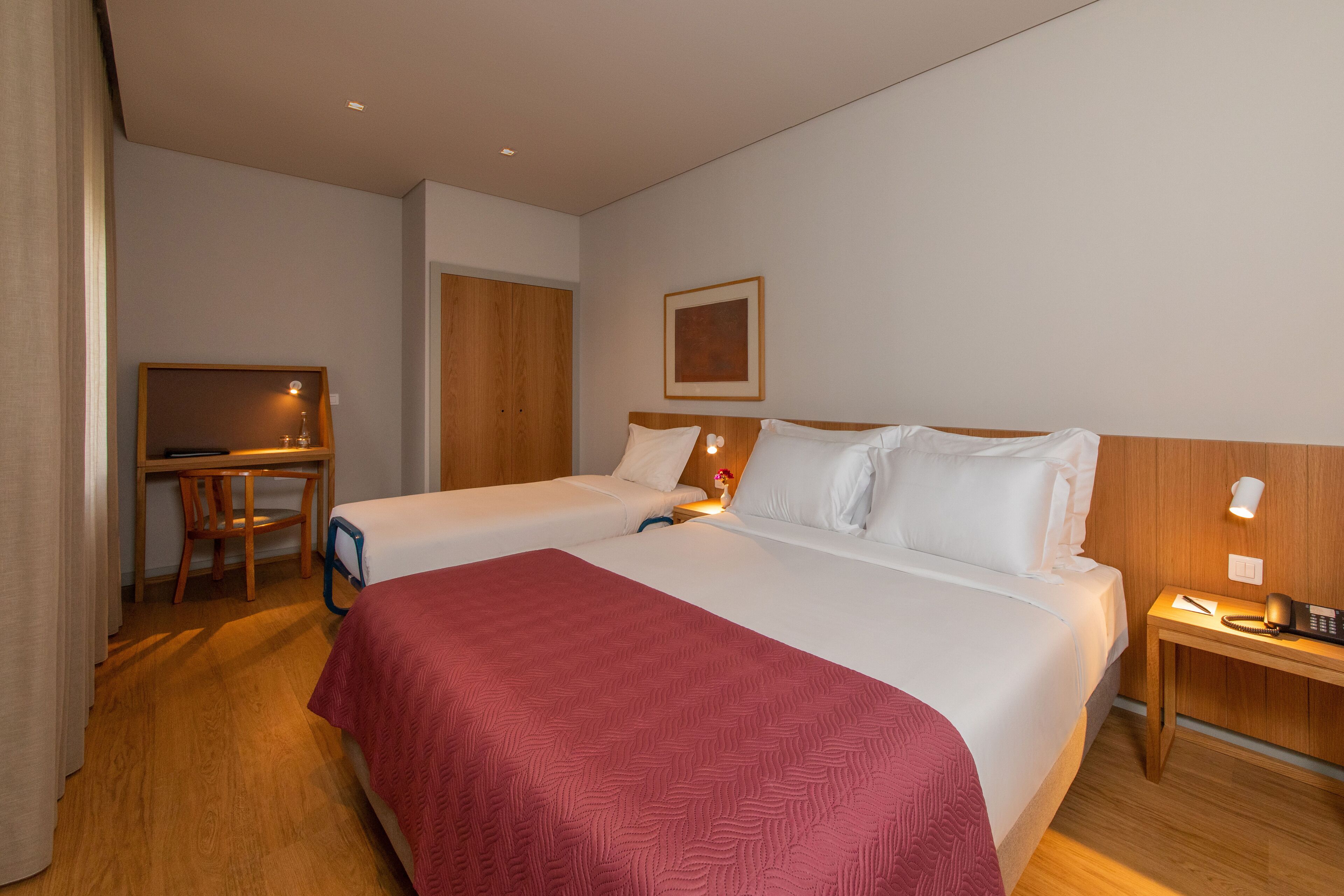 Habitación de hotel con dos camas, un escritorio, una silla, un televisor y una mesita de noche con lámpara.