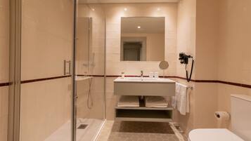 Un baño moderno con ducha envuelta en vidrio, un lavamanos con espejo superior y un inodoro.