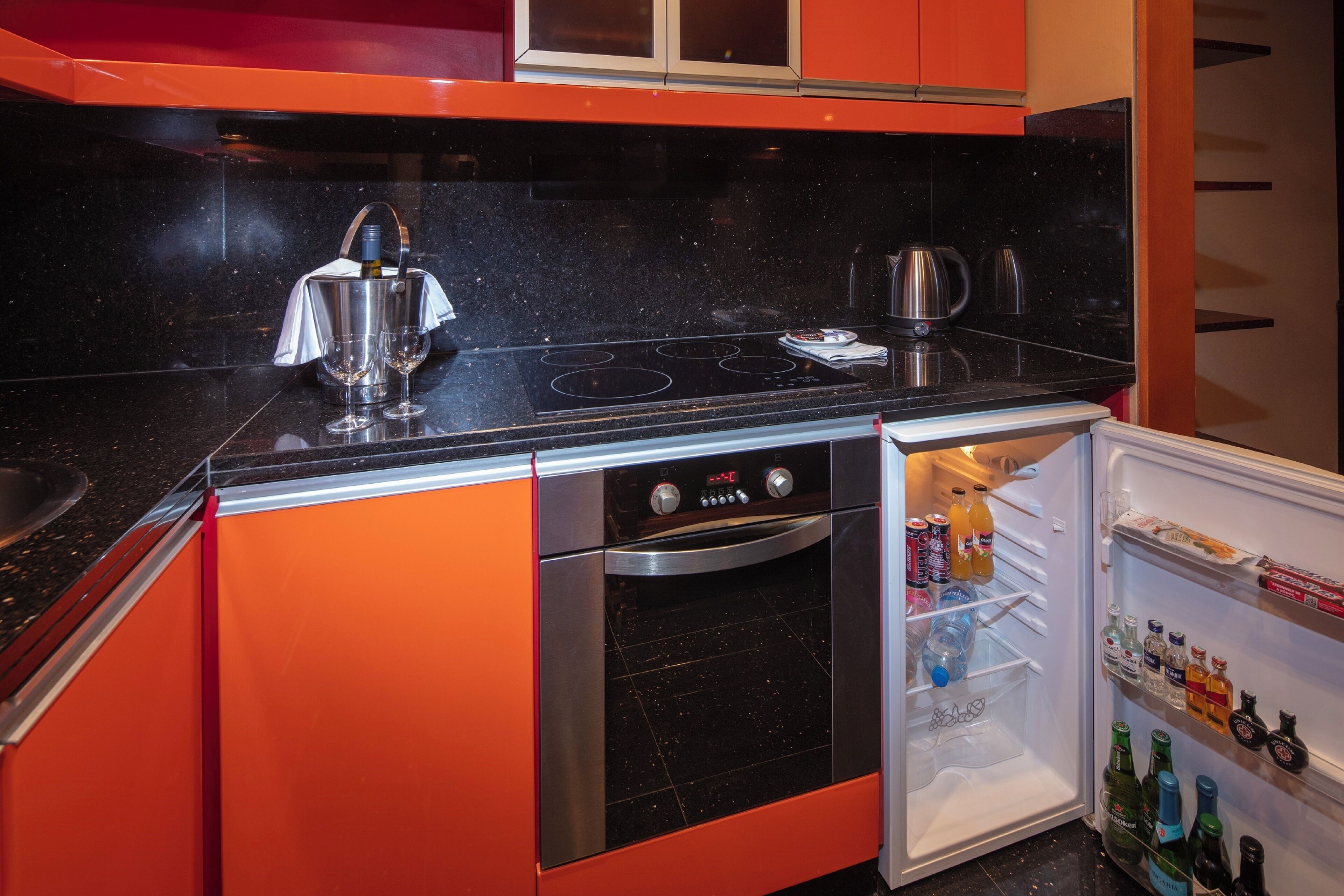 Une cuisine de taille réduite, dotée d’un plan de travail noir, d’appareils électroménagers en acier inoxydable et de meubles de rangement orange.