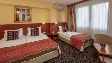 Hotellihuone, jossa on kaksi sänkyä, tuoli, pöytä ja ikkuna, jossa on verhot.