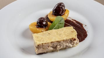 Un plato de postre con una porción de tarta, dos frutas cubiertas de chocolate y una decoración de hoja.
