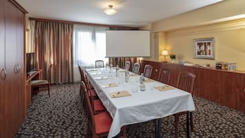 A conference room with a long table, chairs, a projector screen, and a reception area with a counter and refreshments.
