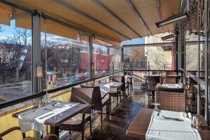 Un restaurante al aire libre con mesas y sillas, amplias ventanas y vista a la calle.