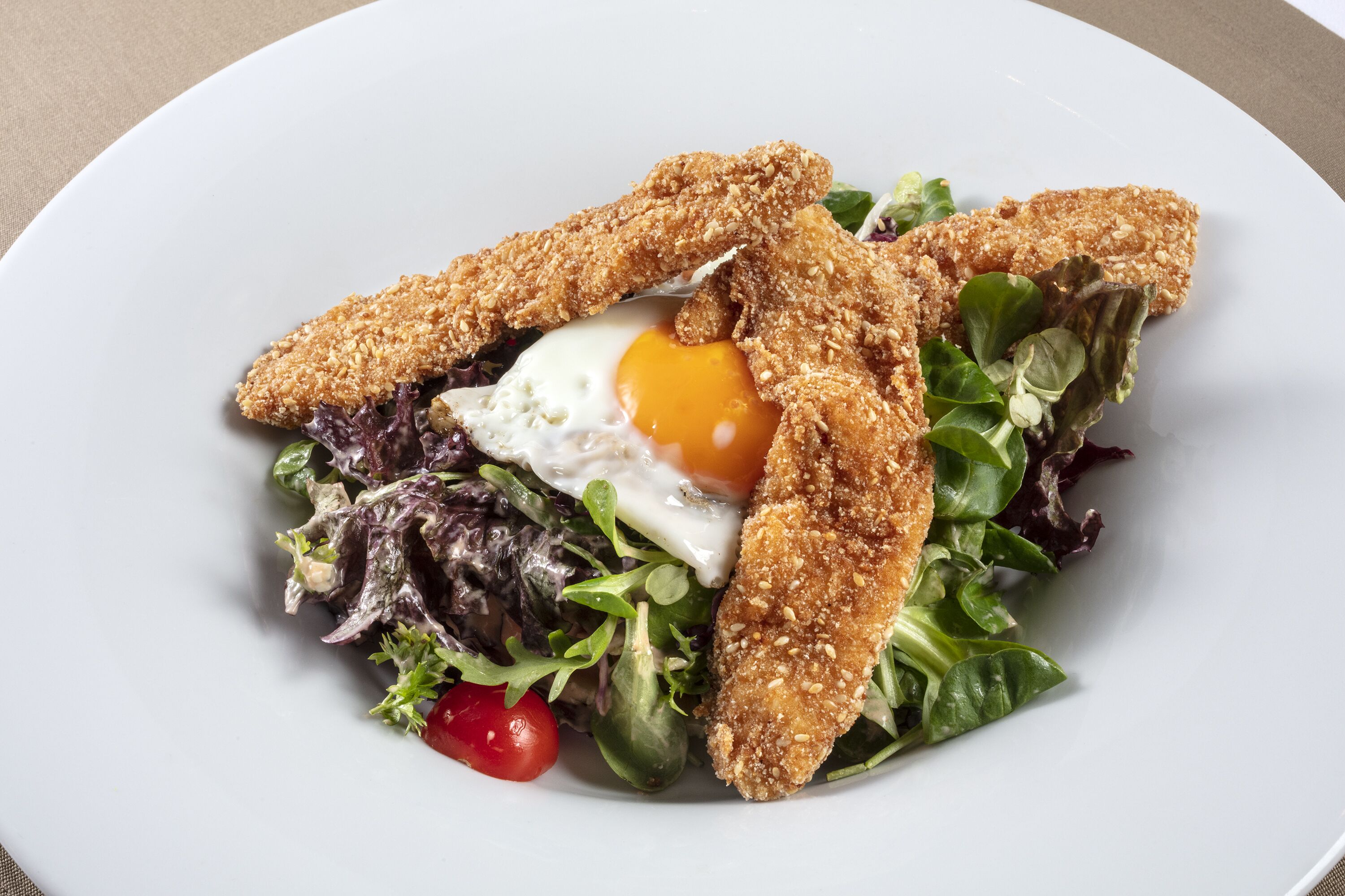 A plate with a salad, egg, and breaded chicken pieces.