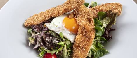 A plate with a salad, egg, and breaded chicken pieces.