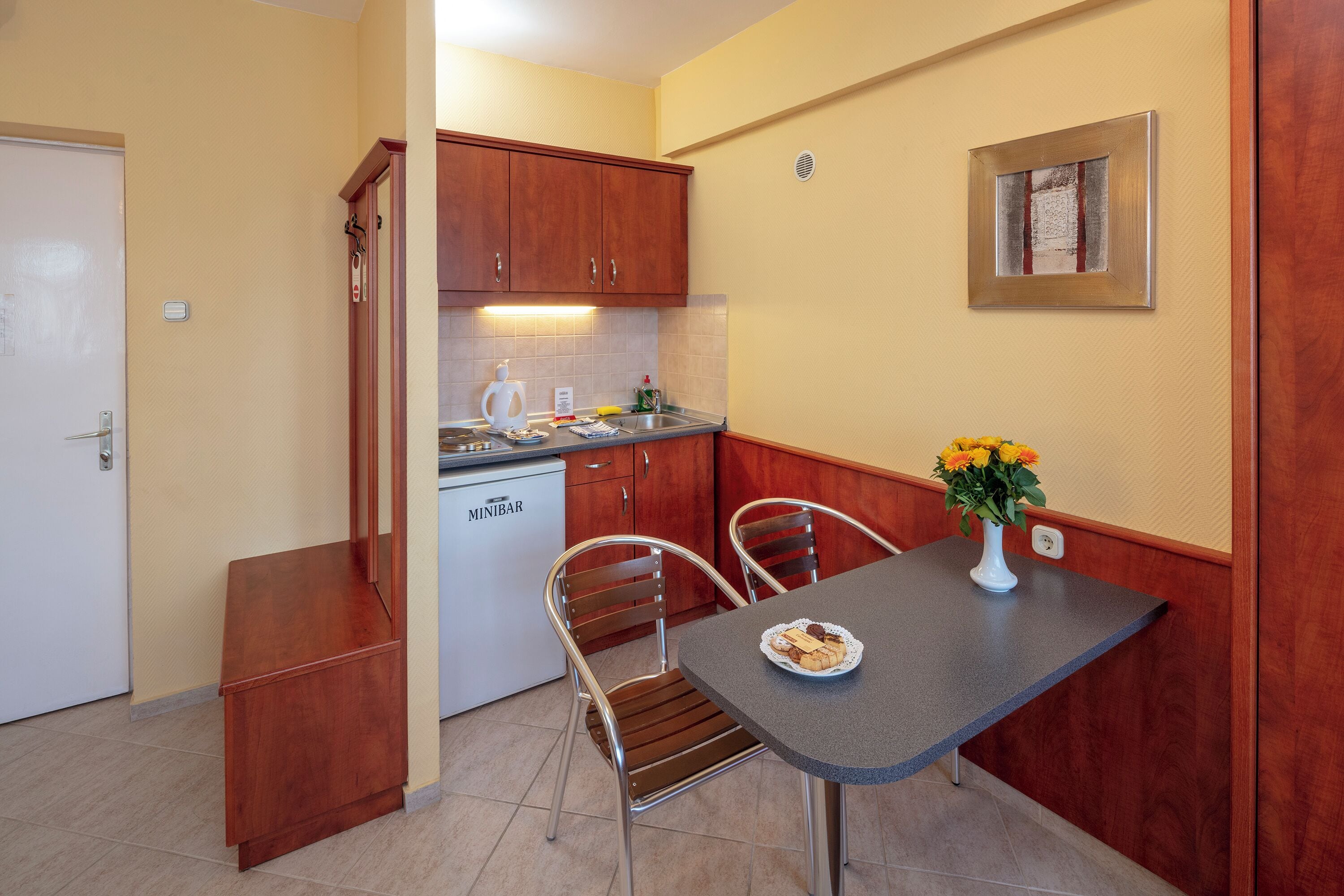 A compact kitchen with wooden cabinets, a built-in dishwasher, and a dining area with two chairs and a table.