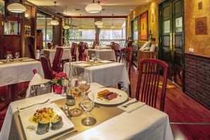 A restaurant interior with multiple tables set for dining, featuring a brick wall and large windows. - Hotel Charles (Budapest)
