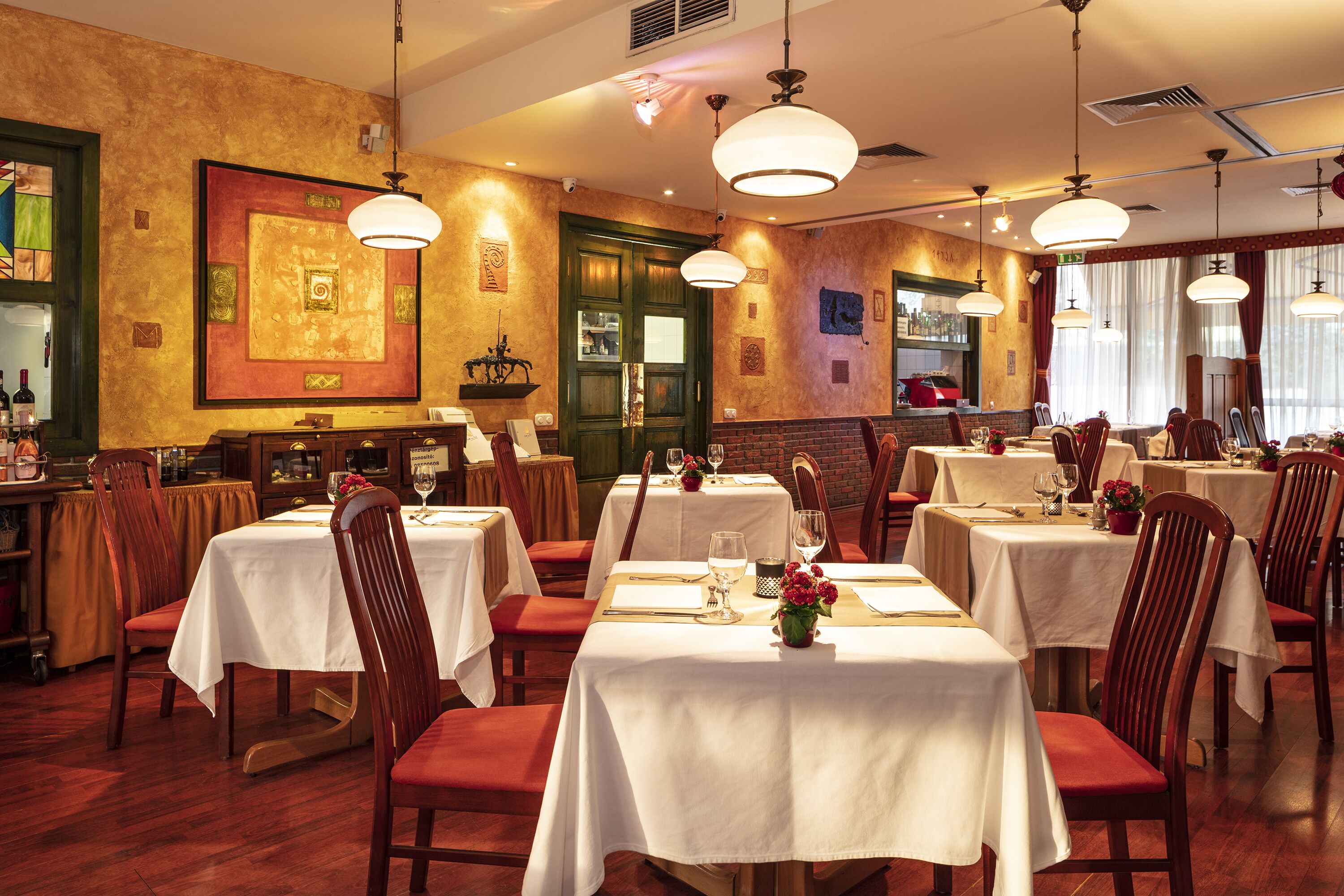 A restaurant with multiple tables set for dining, wooden chairs, and hanging pendant lights.