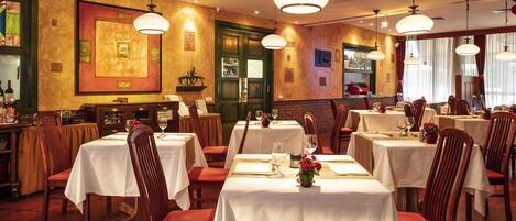 A restaurant with multiple tables set for dining, wooden chairs, and hanging pendant lights.