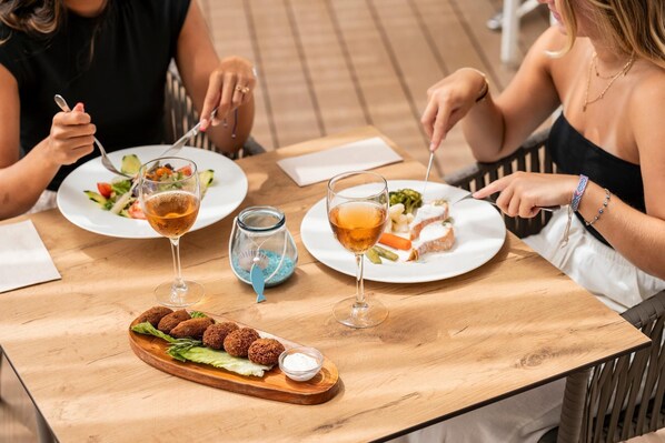 Una mesa de madera con platos de comida, copas de vino y un bol de ensalada.