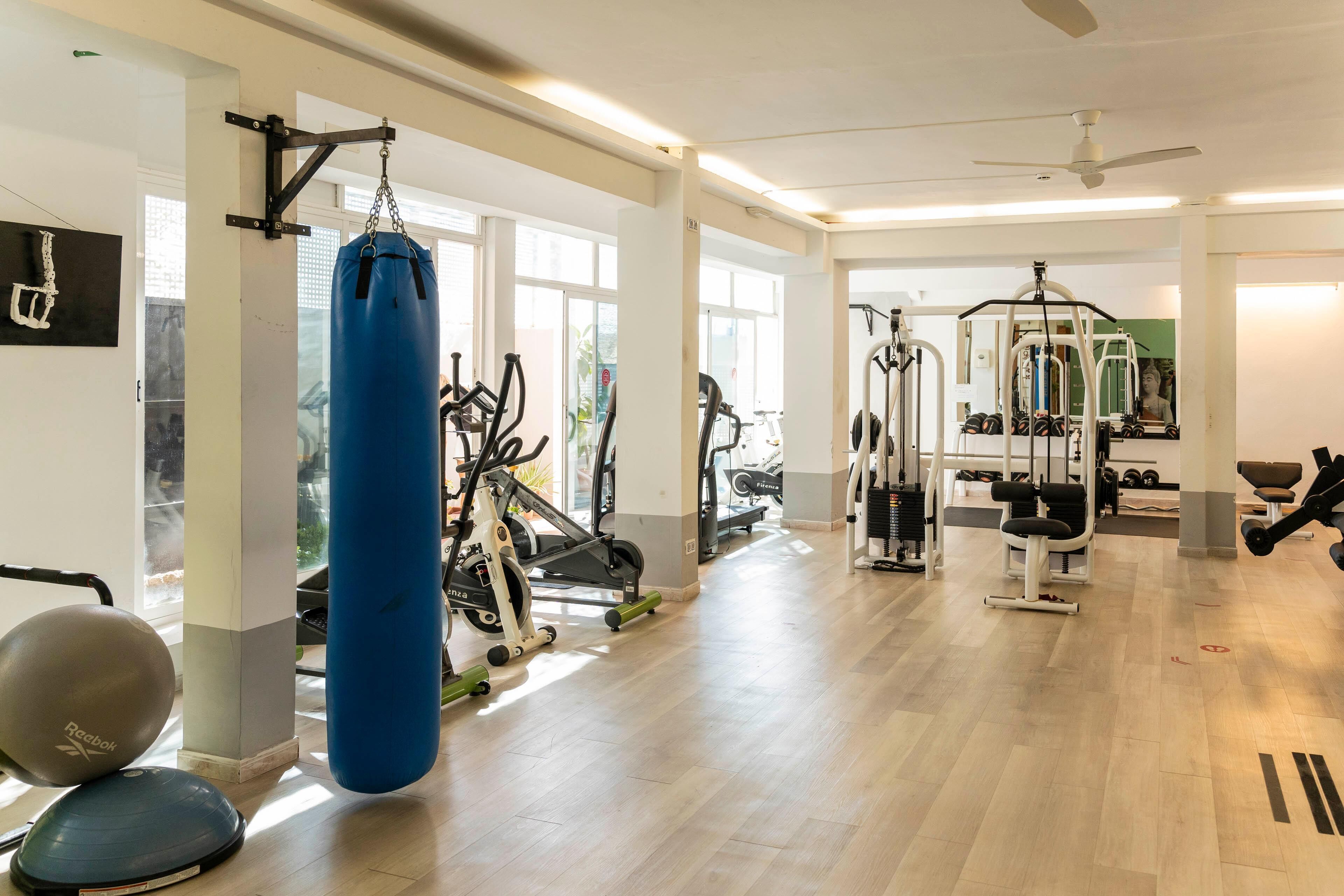 Une salle de sport équipée de machines de cardio, d’appareils de musculation et d’un sac de frappe.