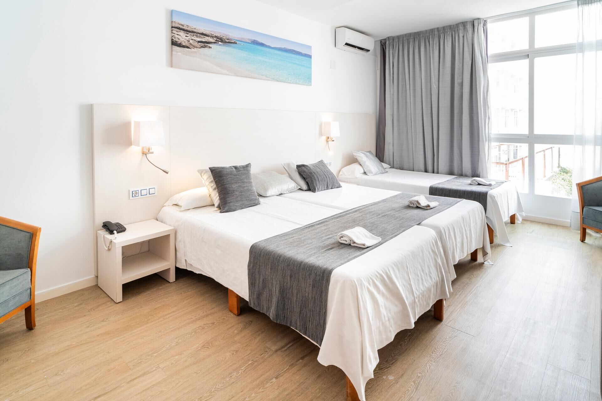 Een hotelkamer met twee bedden, een bureau, een stoel, een telefoon en een raam met gordijnen.