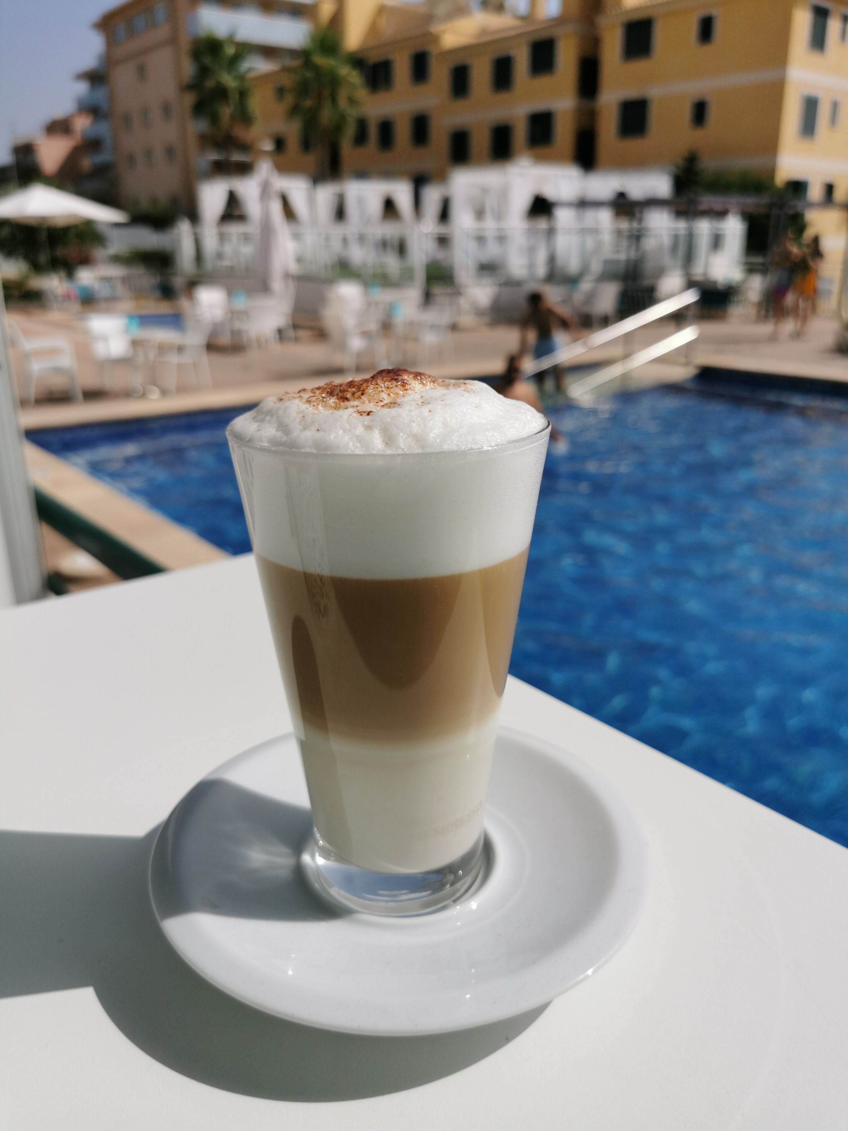 A layered beverage on a white saucer by a poolside.