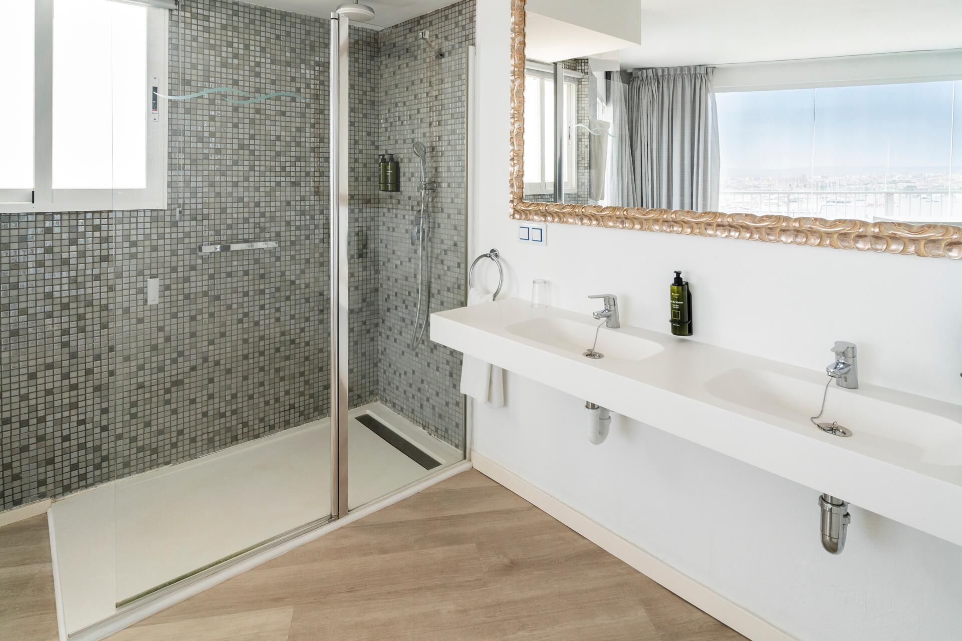 A modern bathroom with a shower, a large mirror, and a view of the city.