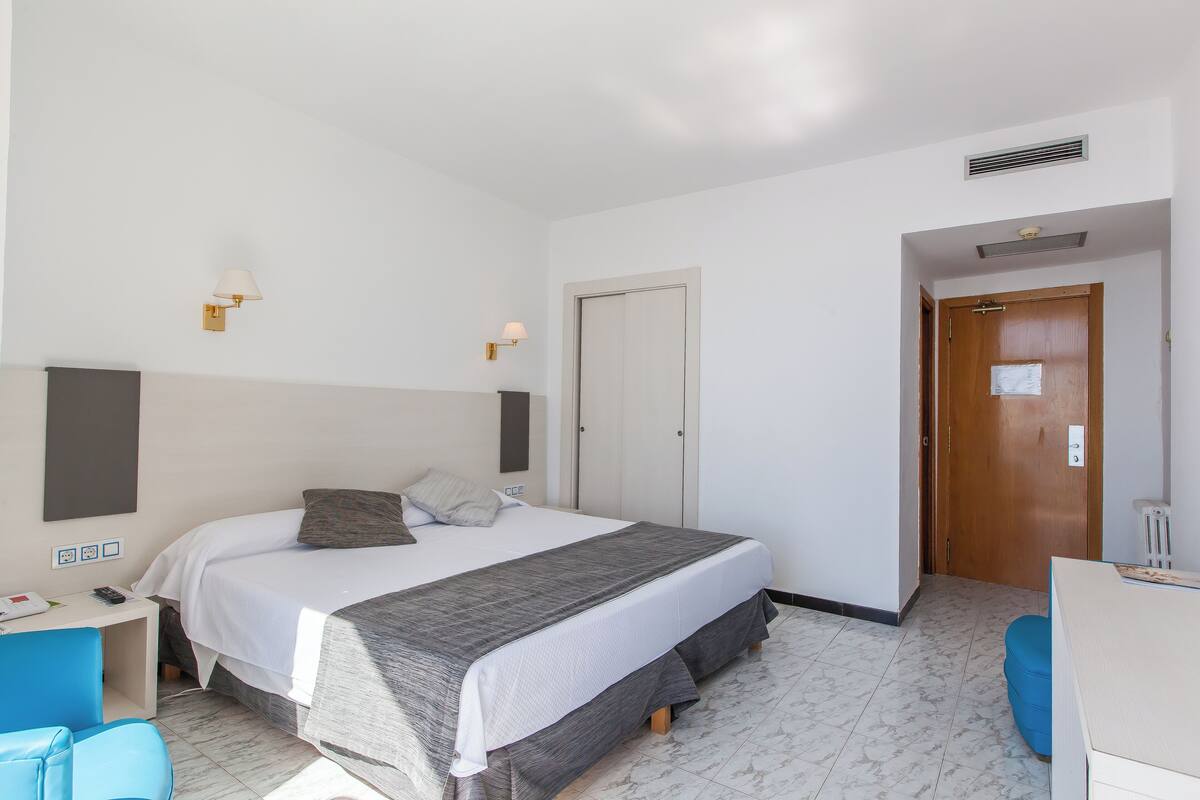 Une chambre d’hôtel avec un lit, une table de chevet, une lampe et une porte.